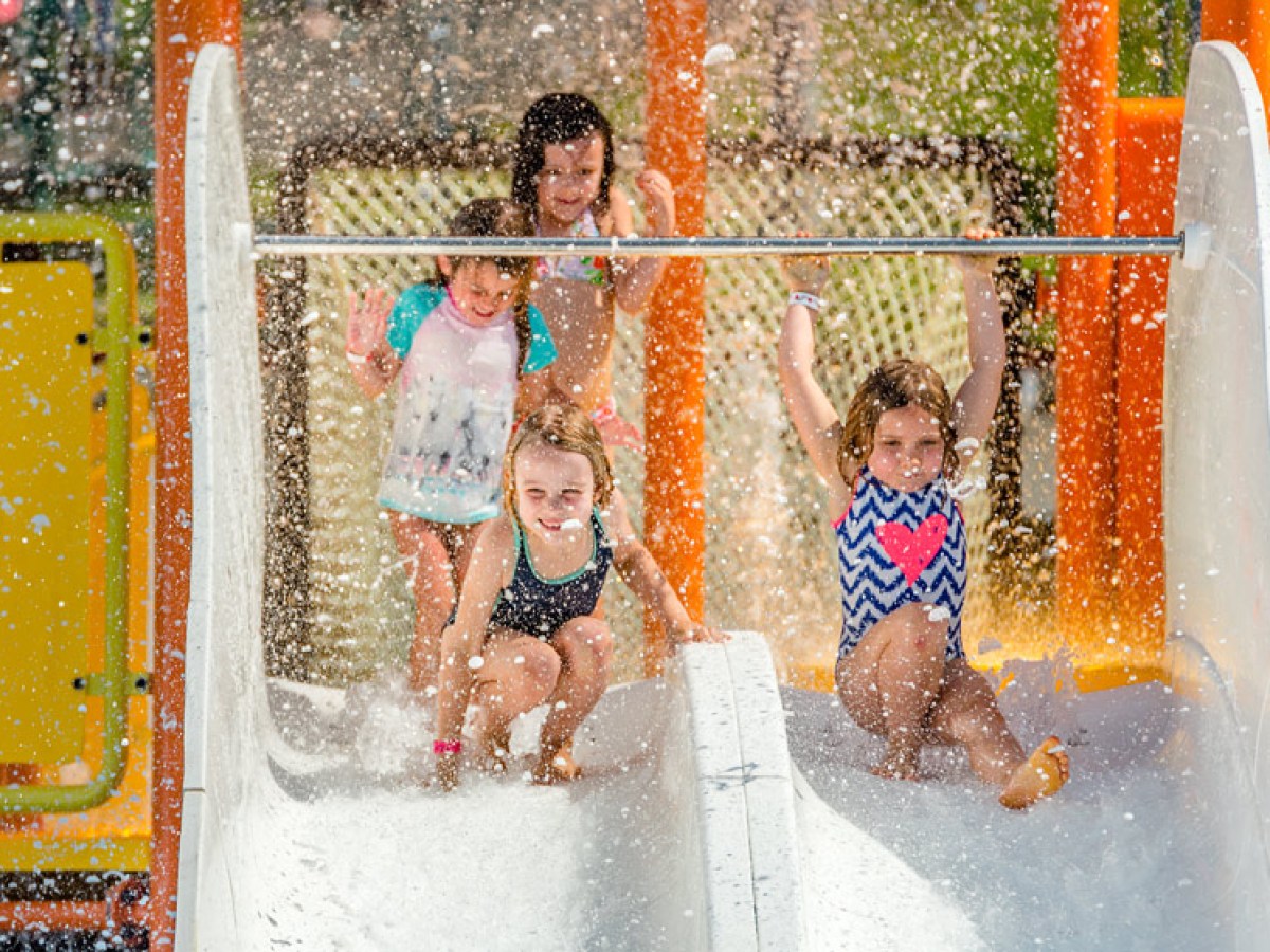 Children playing on a water slide, splashing water in a sunny day.