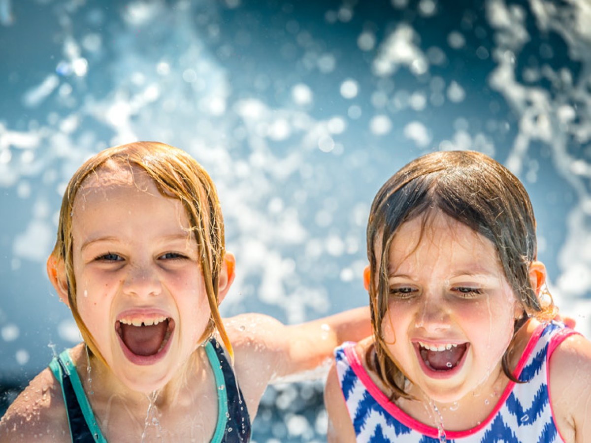 Two children laughing and playing in water fountains.