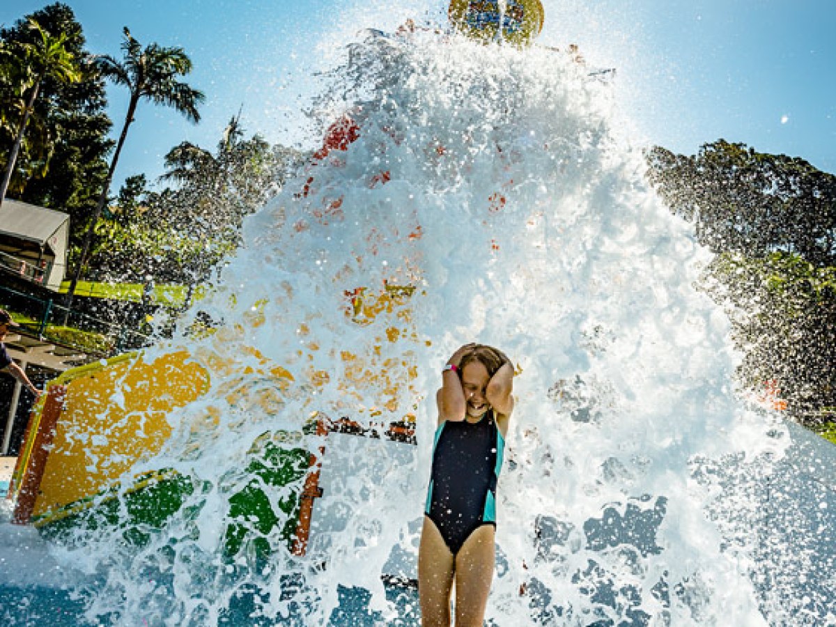 Person playing under a large splash of water at a water park on a sunny day.