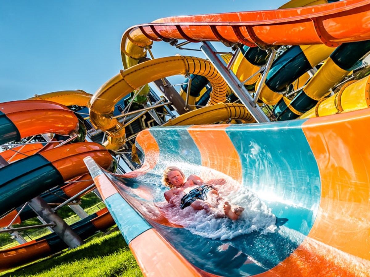 Child sliding down curvy water slide with colorful tubes in background on a sunny day.
