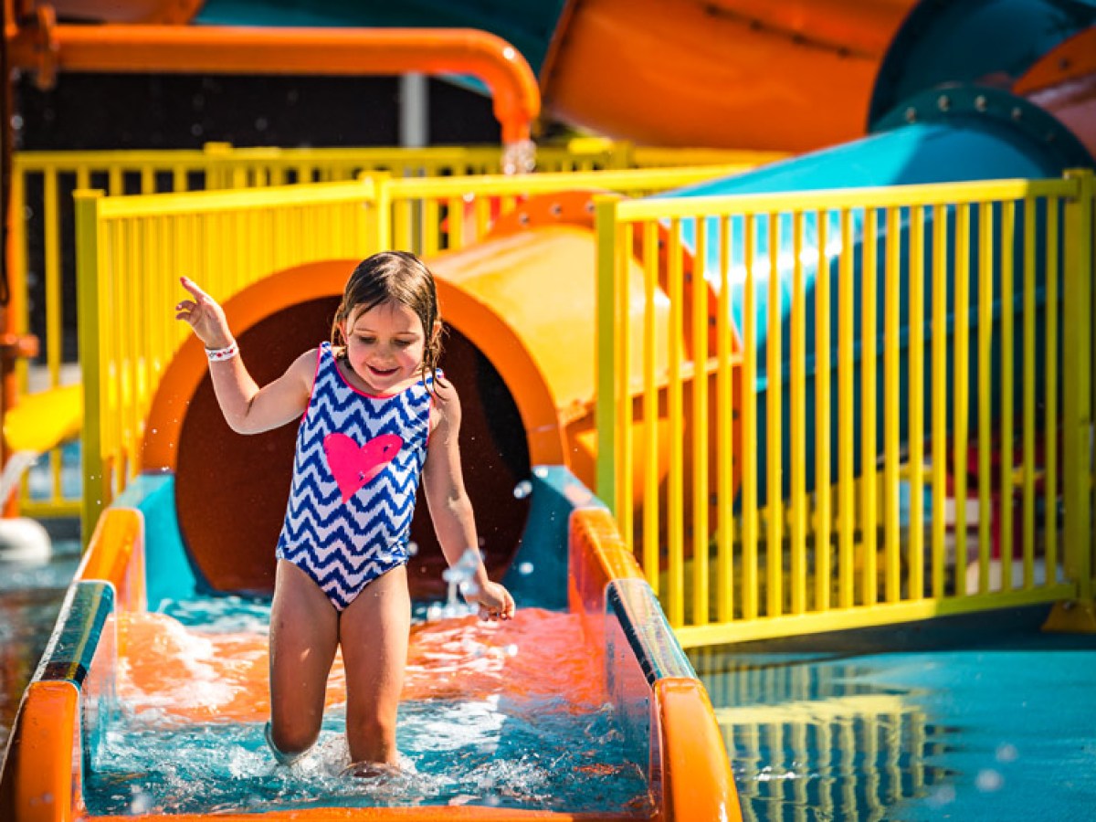 Girl in swimsuit on a water slide at a water park with colorful tubes and fences.