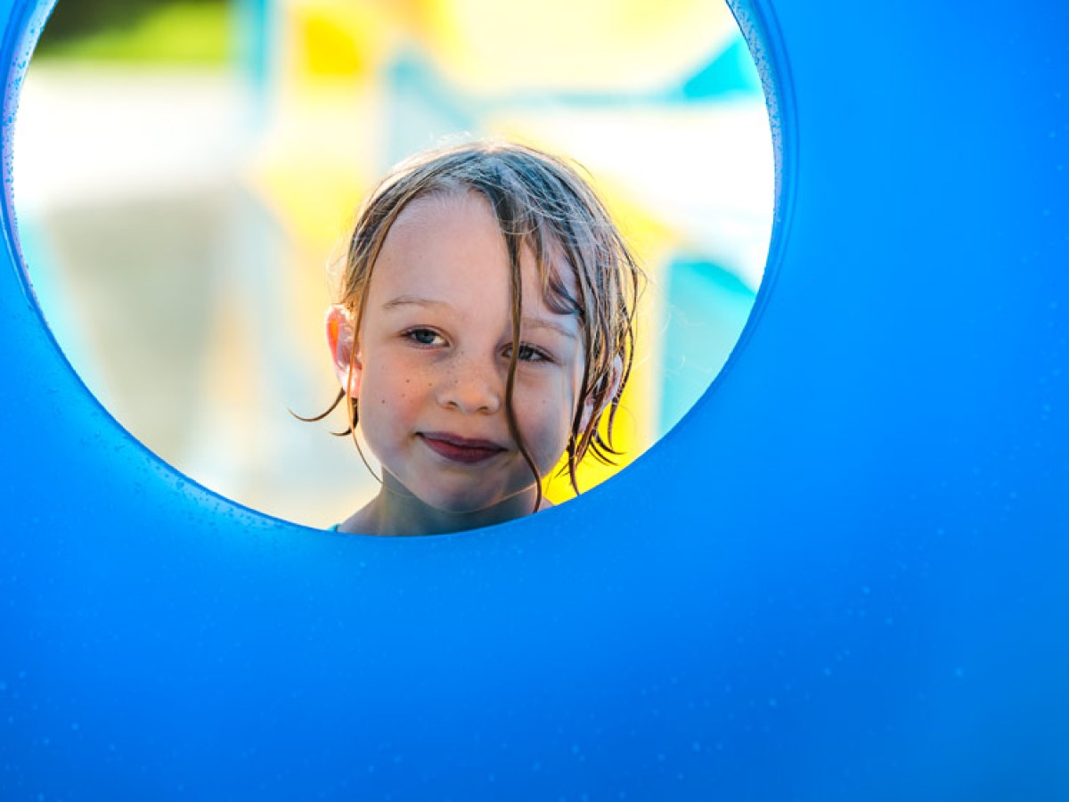 Child's face framed by a circular blue playground hole, smiling slightly.