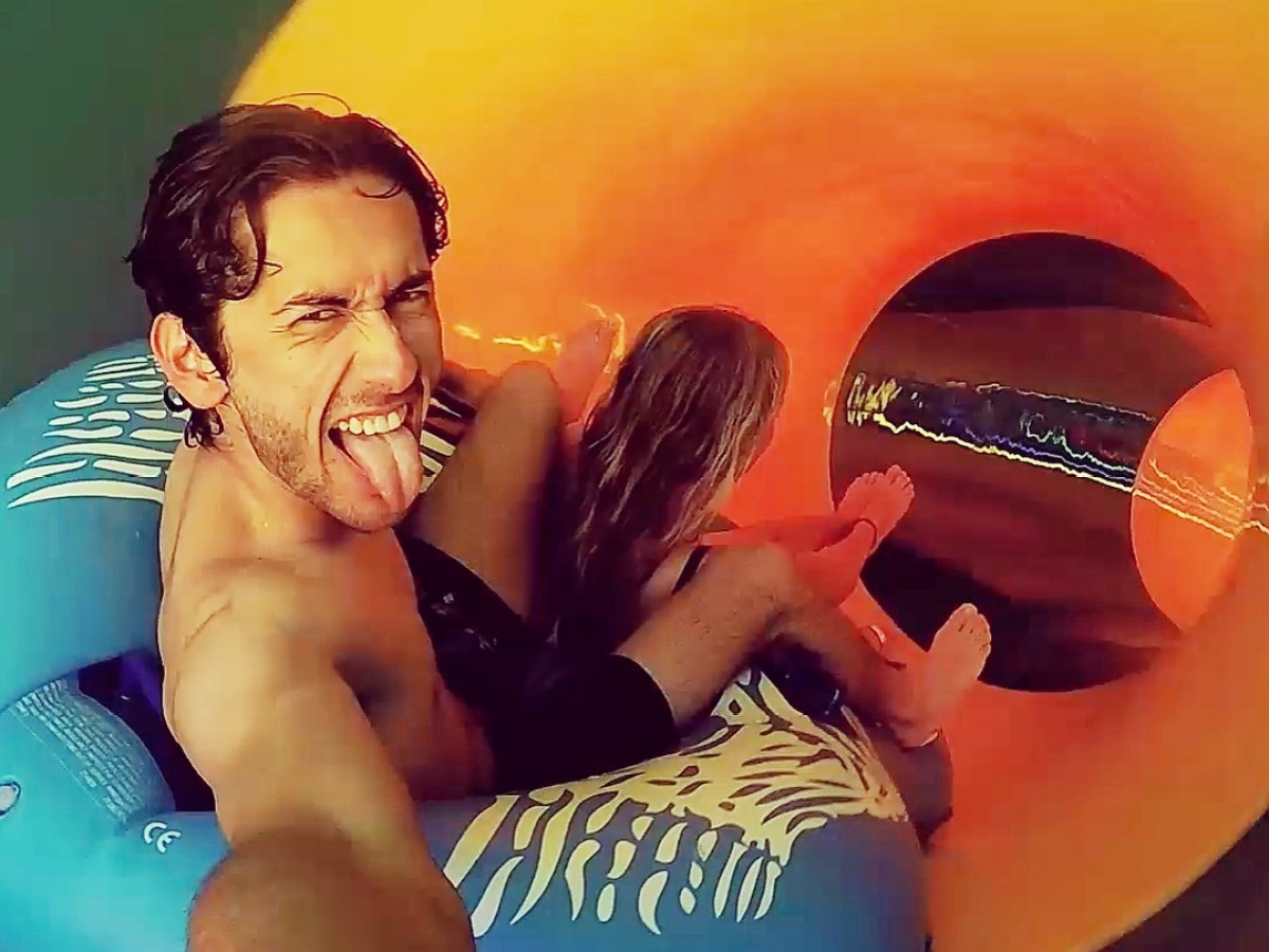 Man and girl on blue tube riding a brightly colored water slide, man making a playful face.