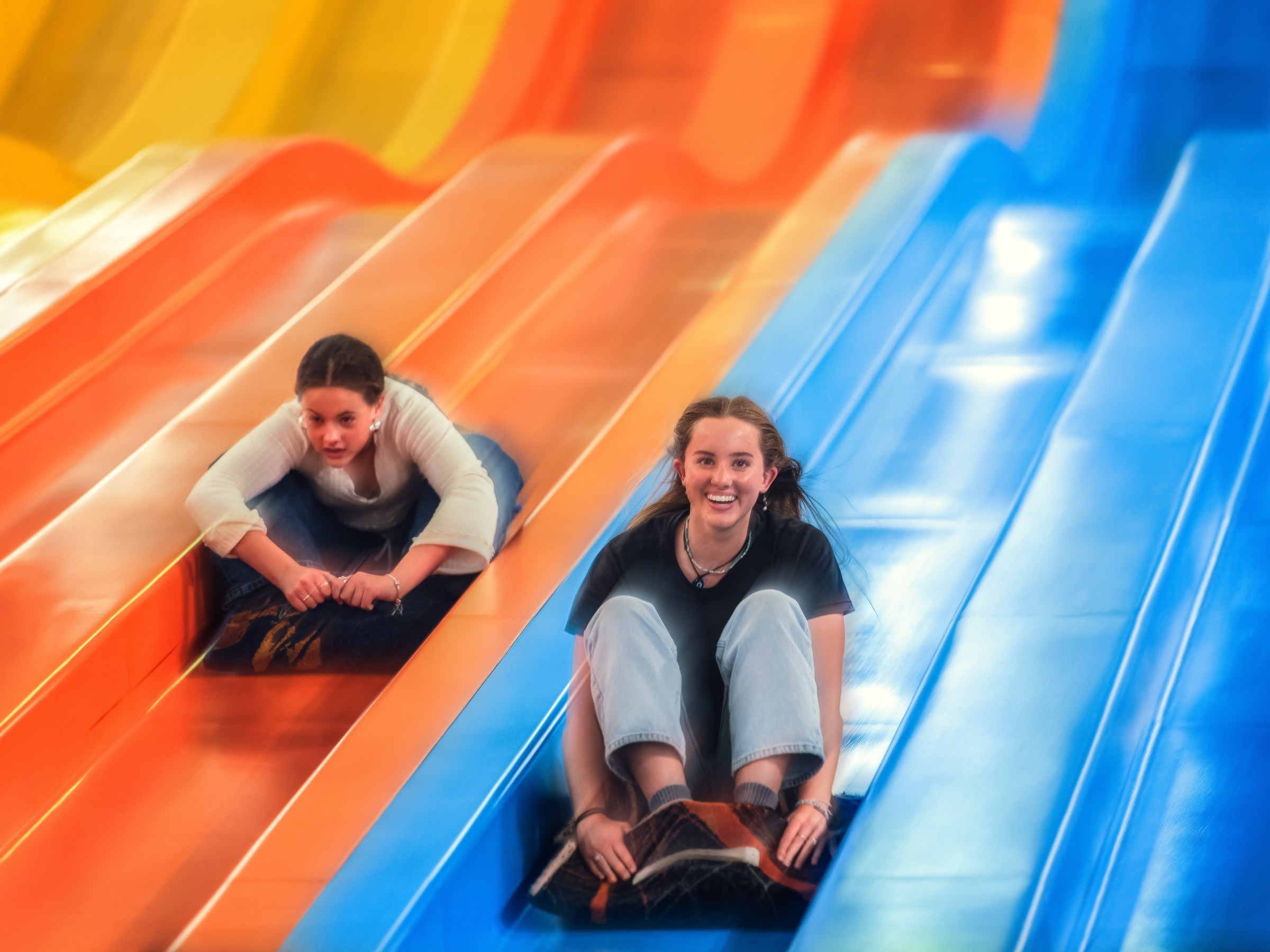 Two people sliding down colorful slides on mats, smiling and having fun.