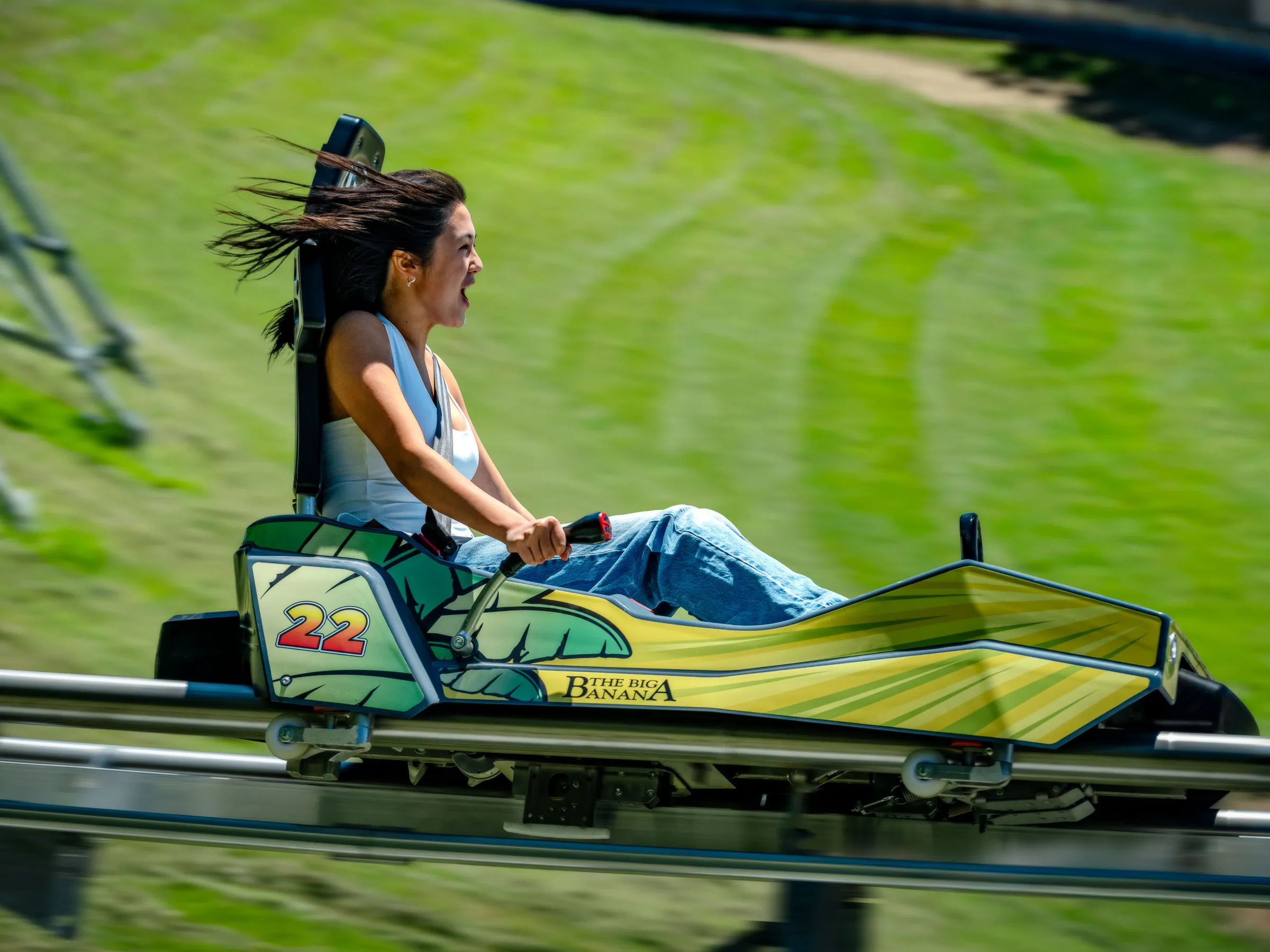 Person enjoying a ride in a yellow roller coaster car on a grassy track.