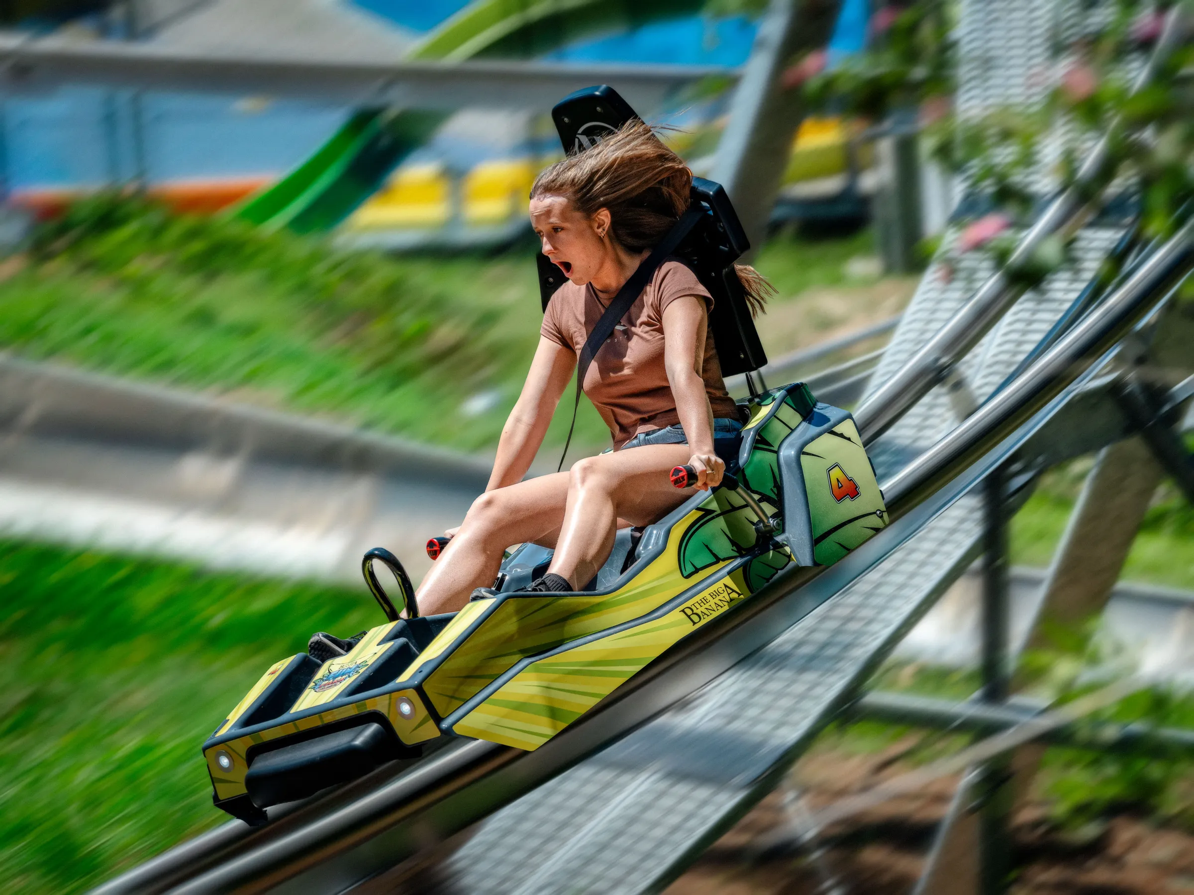 Person riding a fast-moving mountain coaster with an excited expression on a sunny day.