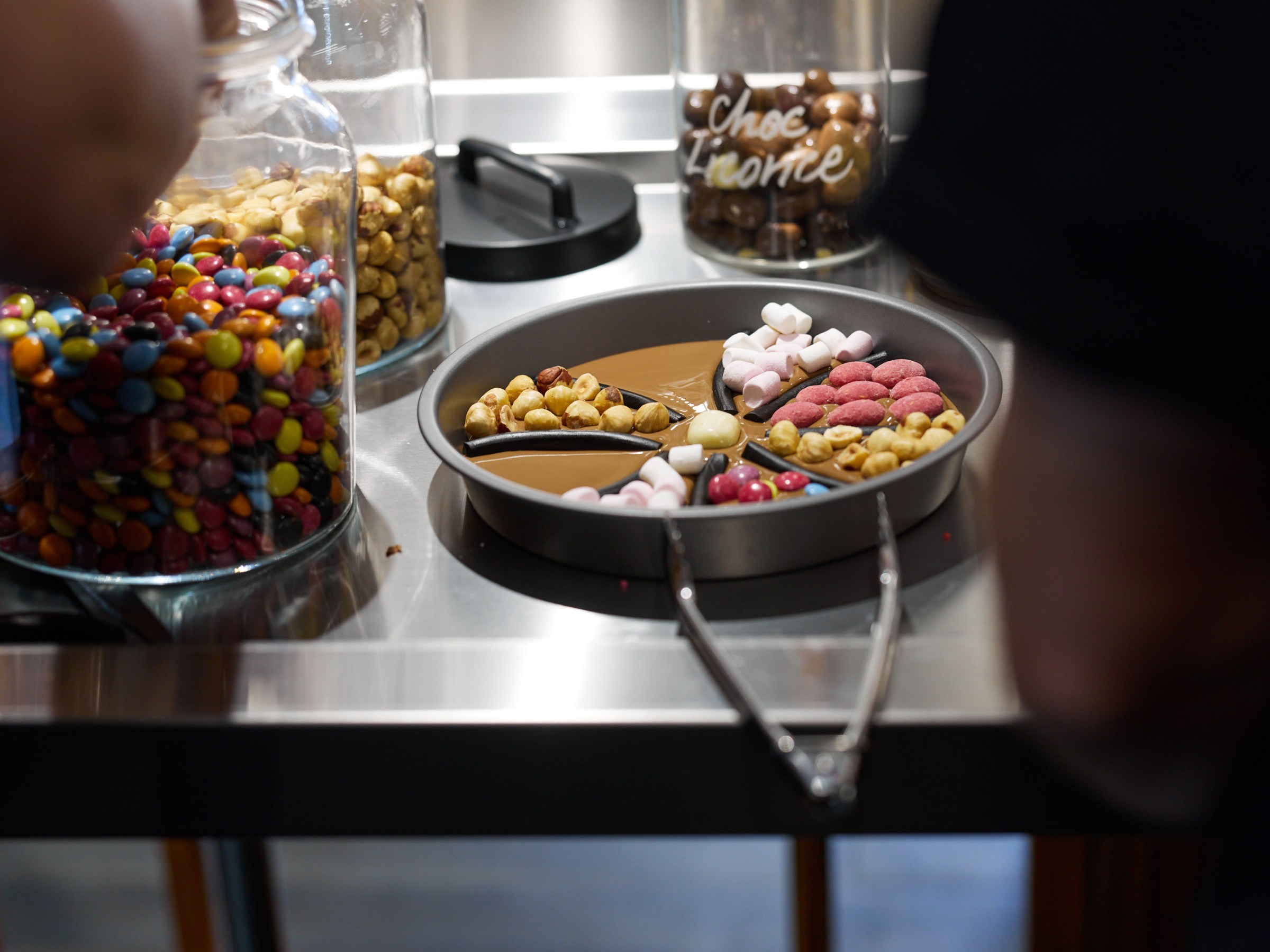 A tray with assorted sweets and snacks, including marshmallows and nuts, on a stainless steel counter.