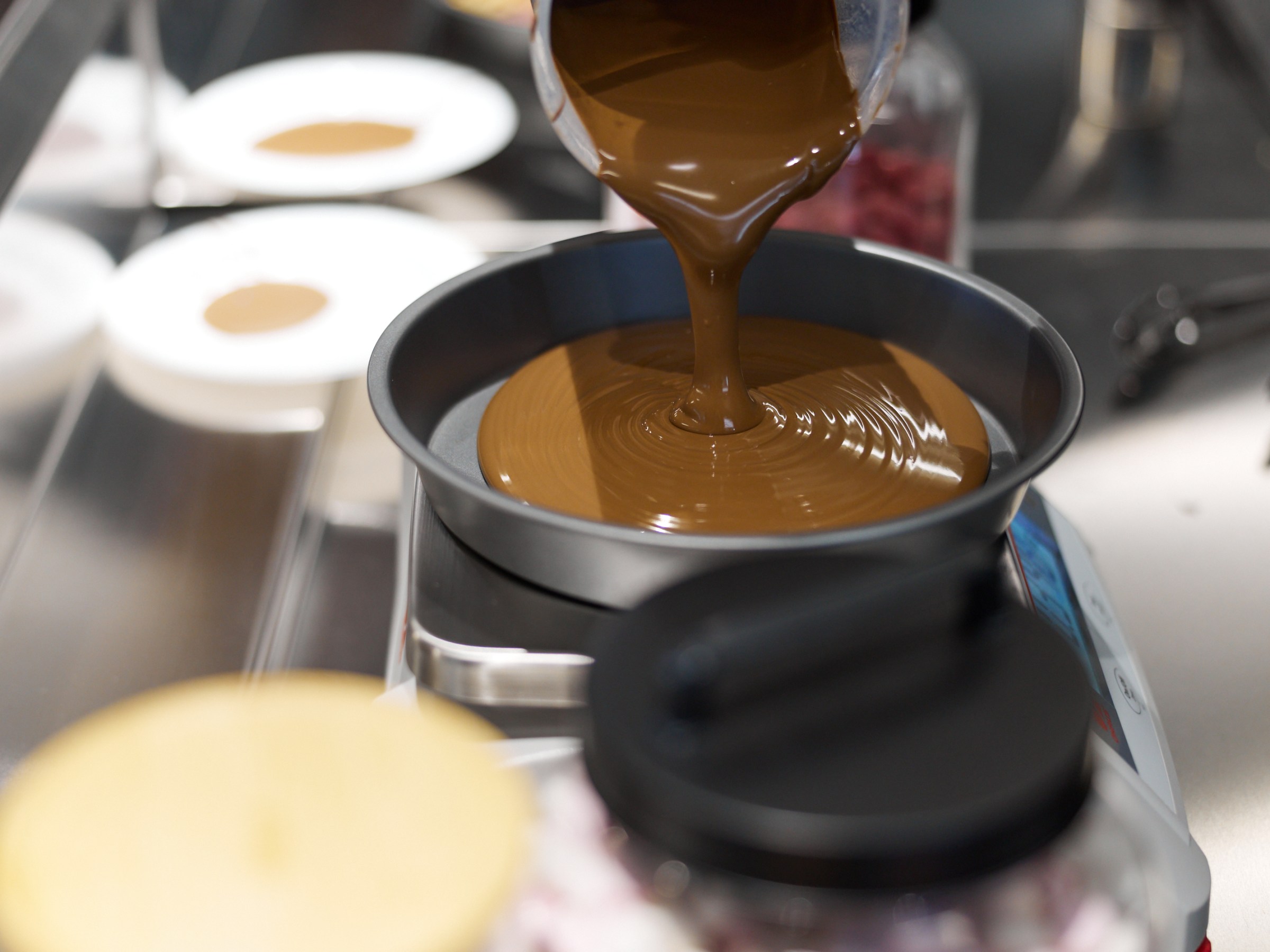 Pouring melted chocolate into a round pan on a kitchen counter.
