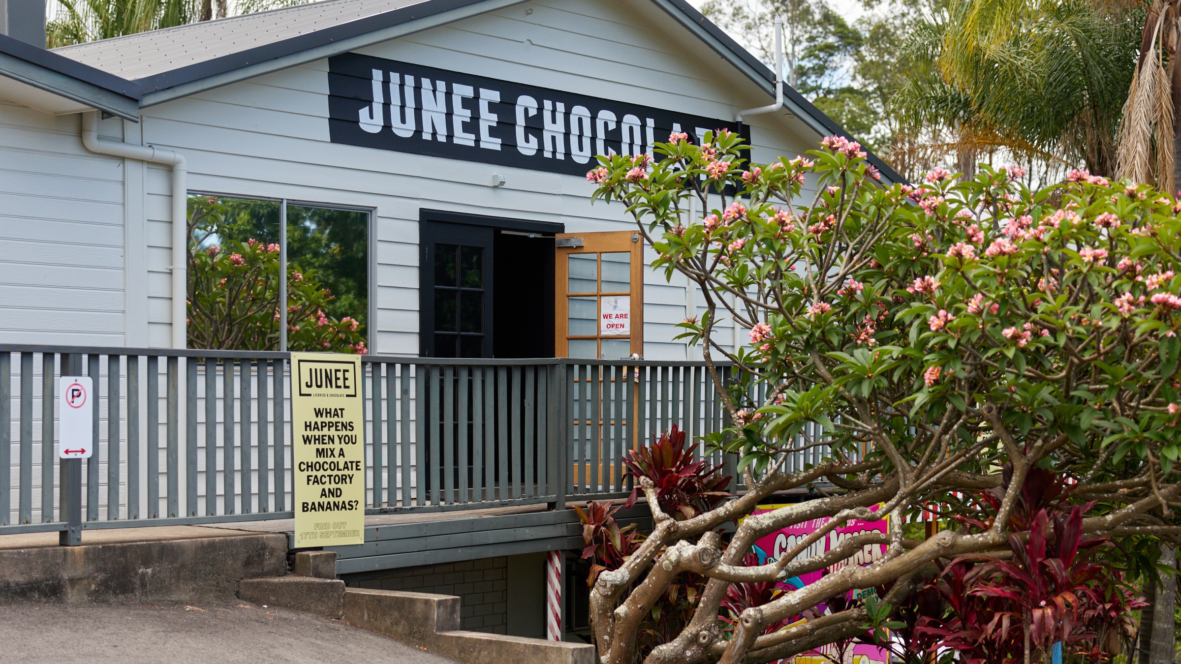 Building with 'Junee Chocolate' sign, surrounded by flowers and trees.