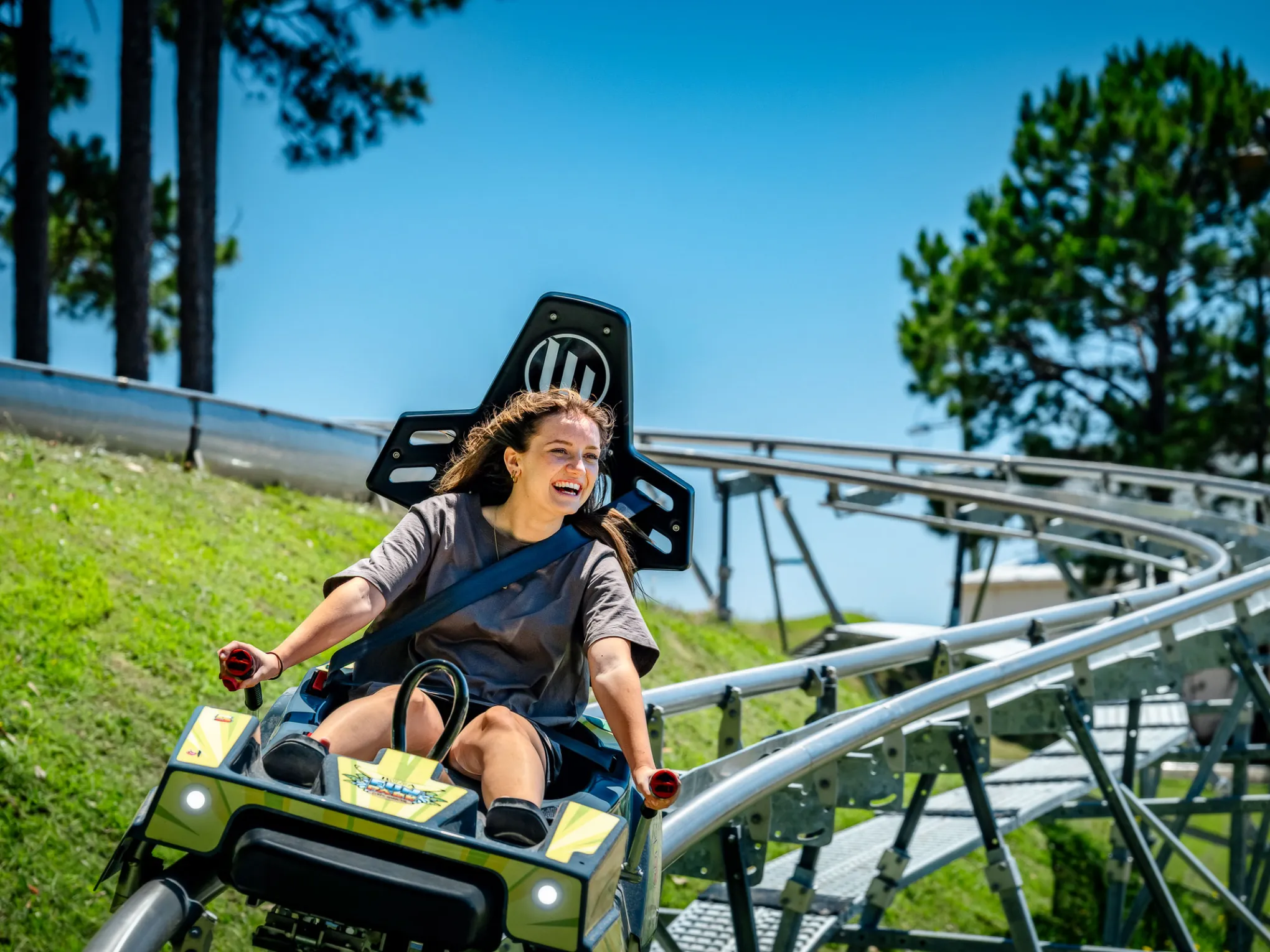 Woman smiling while riding a yellow roller coaster on a sunny day.