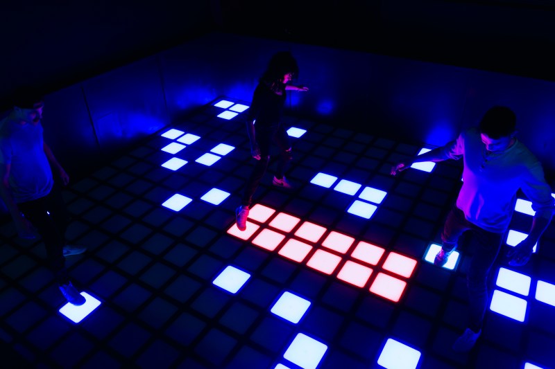 People playing on an interactive floor with illuminated blue and red squares in a dark room.
