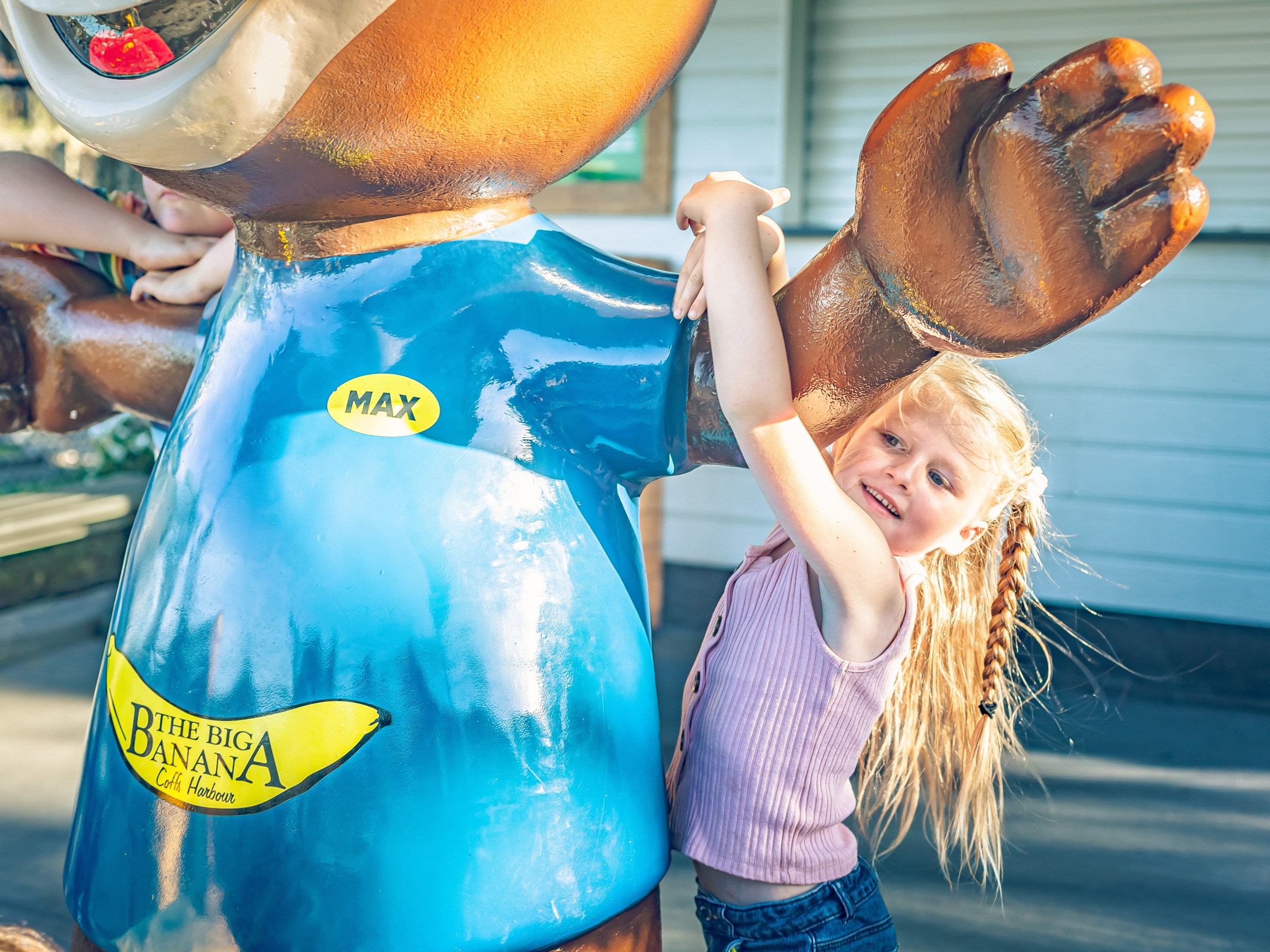 Smiling child hugging a large statue of a bear wearing a blue shirt outdoors.