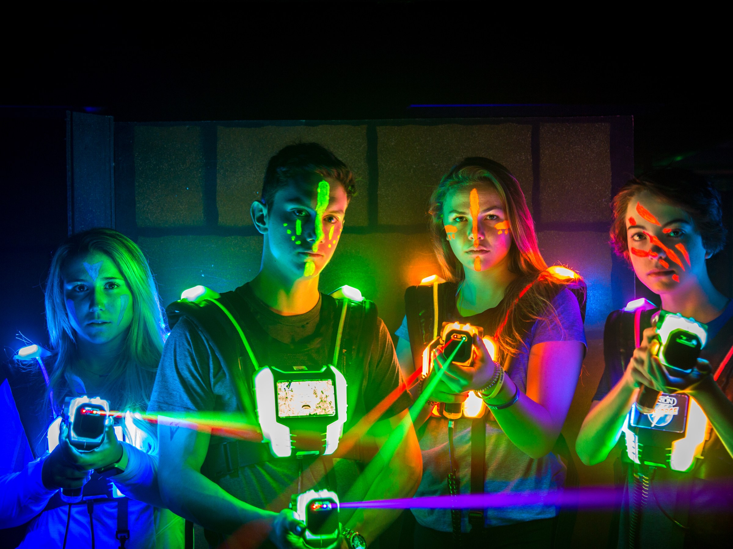Four people playing laser tag, holding laser guns with colorful lights glowing in the dark room.