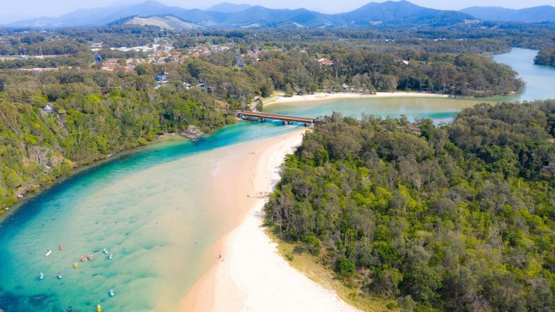 Aerial view of a river meeting the ocean, surrounded by lush greenery and hills.
