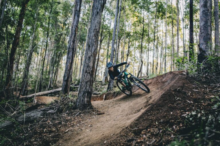 Cyclist riding on a forest dirt trail among tall trees.