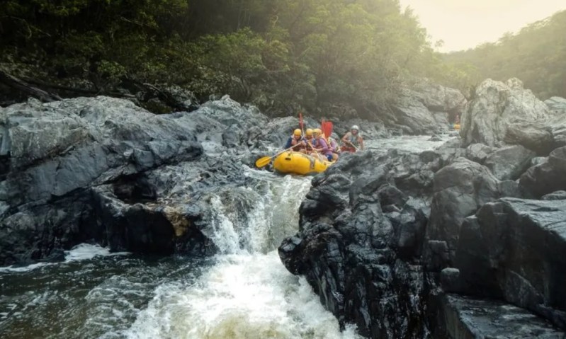 Group rafting down a rocky waterfall surrounded by greenery.