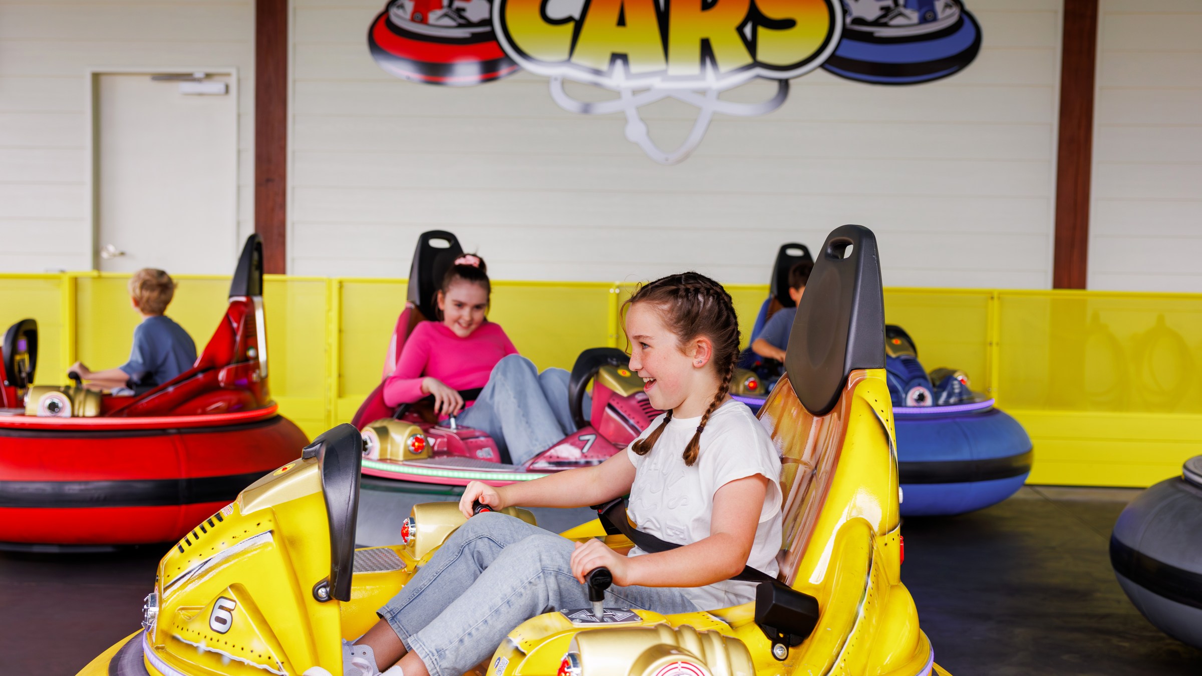 Children ride bumper cars in an indoor amusement space.