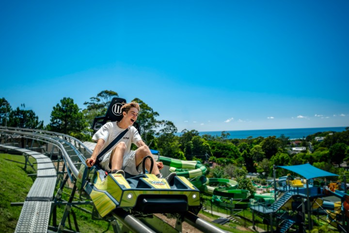 Person enjoying solo roller coaster ride in amusement park with trees and water slides in background.