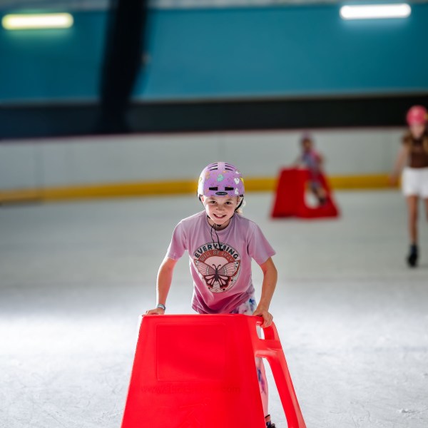 Child in helmet skating with red support on ice rink.